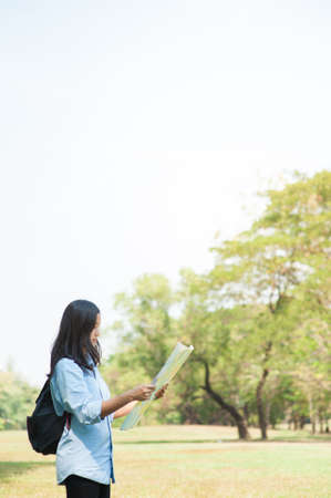 Women traveler with backpack checks map to find directions in the park of Thailand,active people...