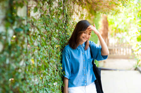 Woman smiling while leaning on wall outdoors ,happy stylish woman hipster standing at green leaves wall, summer travel conceptの写真素材