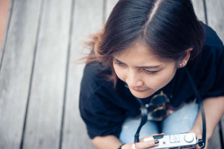 Hipster woman taking photos with retro film camera  on wooden floorof city park,beautiful girl photographed in the old cameraの写真素材