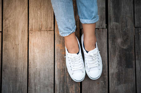 White shoes,Fashion woman's legs with sneakers seated on Wooden floorの写真素材