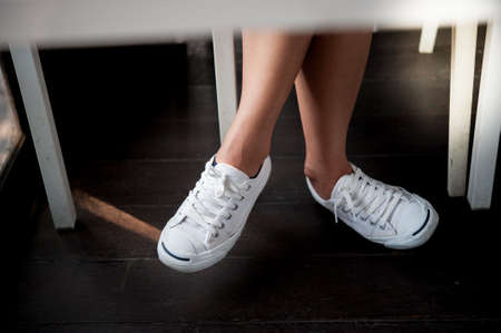 White shoes,Fashion woman's legs with sneakers seated on Wooden floor