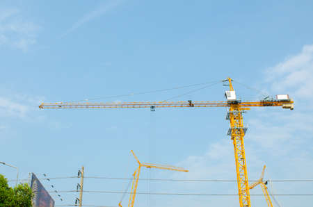 Industrial construction cranes and building silhouettes over sun at sunrise and orange sky backgroundの写真素材