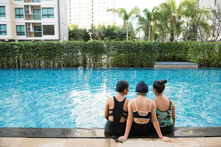 three women friends having fun together in swimming pool together having fun enjoying summer at vacation resort smiling in women holiday conceptの写真素材