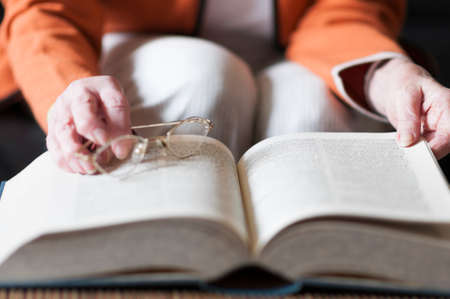 Senior woman reading a book and in her hand she holds a pair of eyeglasses.の写真素材