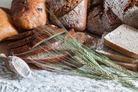 Various types of bread and cereal ears on a wooden table with flour.