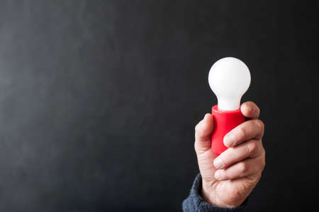 Hand with light bulb against black background with copy space.の写真素材