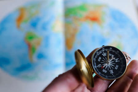 Hand holding compass in front of world map, selective focus.の写真素材