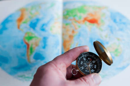 Hand holding compass in front of world map, selective focus.