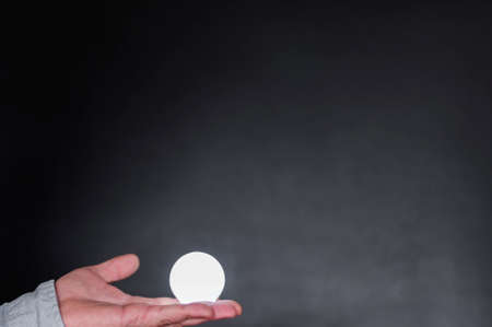 Hand with light bulb against dark background with copy space.