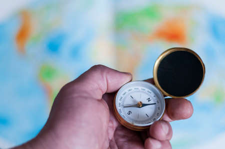 Hand holding compass in front of world map, selective focus.の写真素材