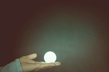 Hand with light bulb against dark background with copy space.の写真素材