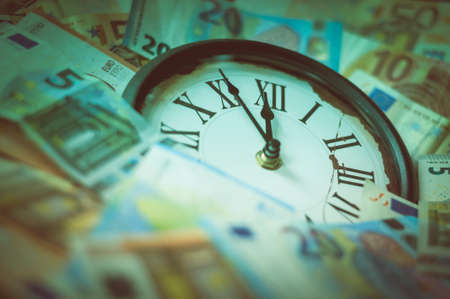Euro currency and a clock, the hands stand five minutes before twelve.の写真素材