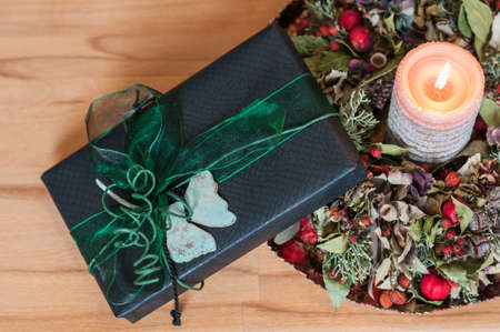 Gift in black paper with green bow and luminous candle in front of wood background.の写真素材