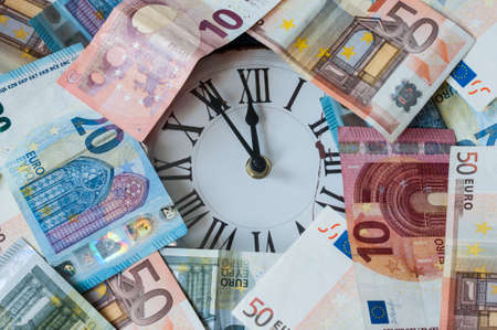 Euro currency and a clock, the hands stand five minutes before twelve.
