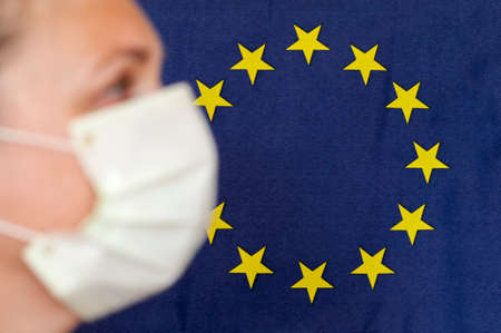 Woman with face mask in front of European Union flag in profile.
