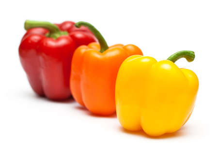 three different color peppers in a row on white background 
