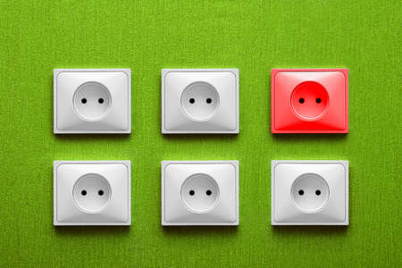 Five white and one red electric sockets in a green wallの写真素材