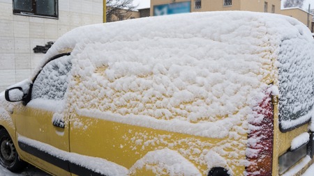 Frozen car compact yellow van covered snow at winter day. Urban scene of city life in winter time in snow stormの写真素材