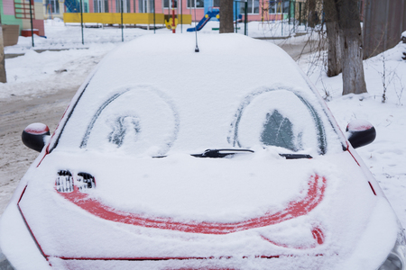 Frozen car windshield covered with ice and snow on a winter day. drawn eyes and a smile.の写真素材