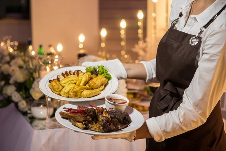 Waitress is carrying two plates with meat dish. Restaurant catering servicesの写真素材