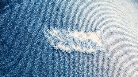 Texture of blue jeans jeans with fashionable hole.