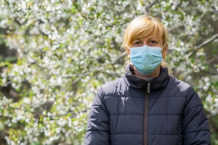 A girl in rubber gloves and medical mask against the background of a flowering tree. The concept of protection from COVID-19 coronavirus infection.の写真素材