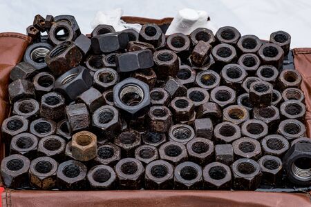 Lots of big black nuts from bolts nicely stacked in a box.