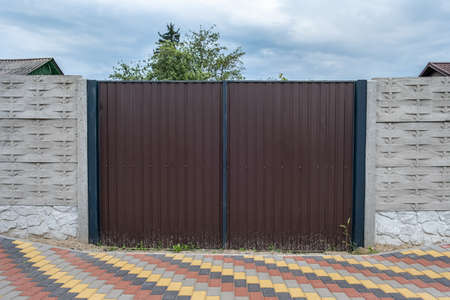 The brown gate of corrugated iron between the concrete slabs of the fence.