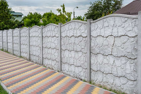 Decorative concrete fence on the background of green trees.