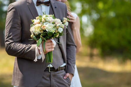 The groom in a wedding suit holds a beautiful wedding bouquet of roses in a pink shade.の写真素材