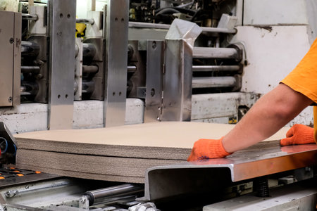 Enterprise for the production of cardboard containers . Worker put sheets of cardboard in a machine...