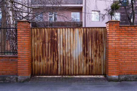 An old rusty metal corrugated gate between the brick pillars in front of the apartment building.の写真素材
