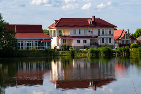 A modern two-storey house with a red tiled roof on the shore of a lake with a reflection in the water.の写真素材