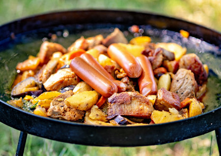 Portable grill is cooking sausages and cut up meat.の写真素材
