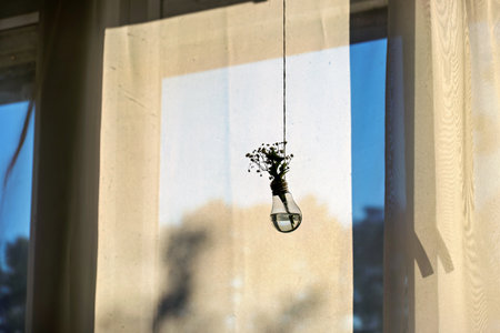 Light bulb hanging from window next to window sill with flowers in it.の写真素材