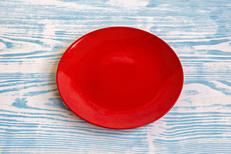 This is an image of a red plate placed on a surface with a blue and white striped patternの写真素材