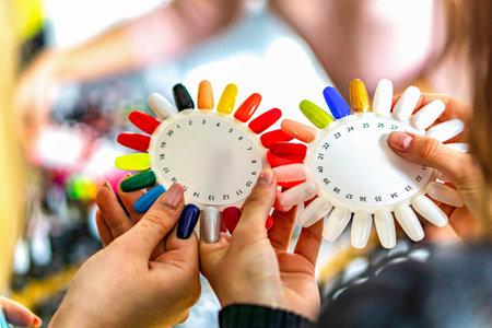 This image shows two hands holding circular objects with a colorful array of nail polish bottles attached to themの写真素材