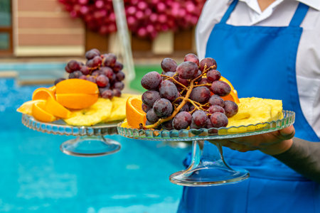 In the image there is a person holding two glass plates with a variety of fruits