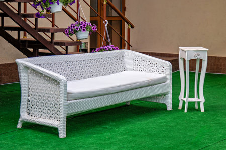 This is an image of a white wicker sofa with a cushioned seat placed on a green artificial grass...