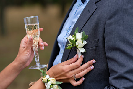 A man and woman are holding hands with the man wearing a suit and the woman holding a glass of...