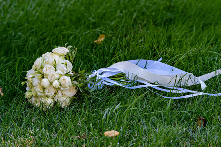 A bouquet of white roses with greenery and a blue ribbon on a grassy fieldの写真素材
