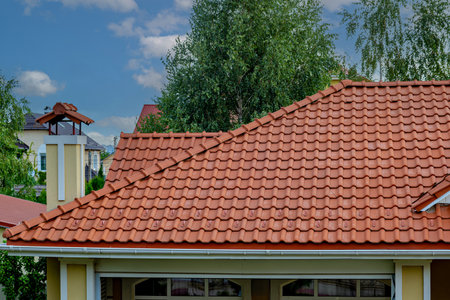 A house with a red tiled roof and a chimney set against a backdrop of trees and a partly cloudy sky