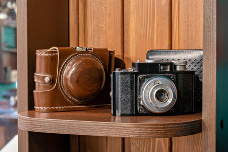 A vintage camera and a brown leather camera case on a wooden shelf