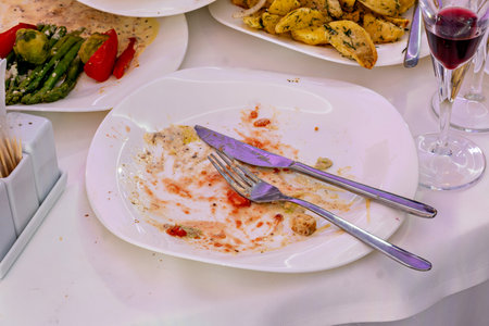 A plate with a knife and fork partially eaten food and a glass of red wine