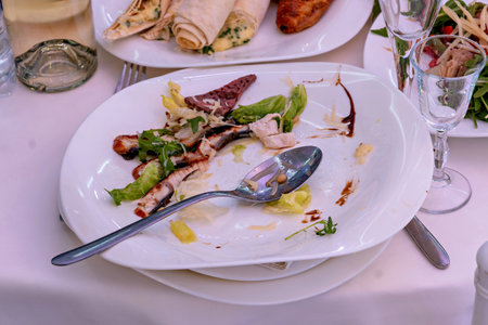 A plate of food with a spoon on it sitting on a table with other plates and glassesの写真素材