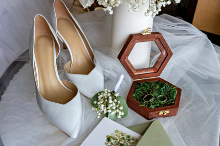 A collection of wedding items on a table including a pair of white high heels a bouquet of flowers a...