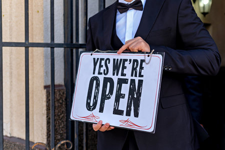 A man in a suit holding a sign that says YES WE'RE OPEN