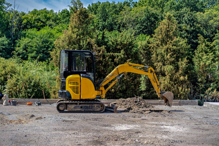 A yellow excavator parked on a dirt lot with a pile of dirt in front of it.の写真素材