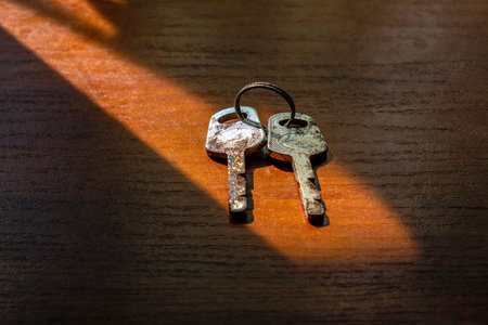 Two old, rusty keys with silver and black finishes lie on a wooden surface with a shadow..