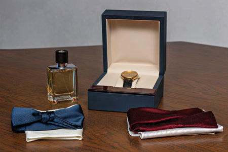A blue box with a gold watch inside sitting on a wooden table with two blue bow ties and a red scarf.の写真素材